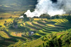 Beautiful aerial shot of terraced rice fields with smoke wafting over them in the early morning light.