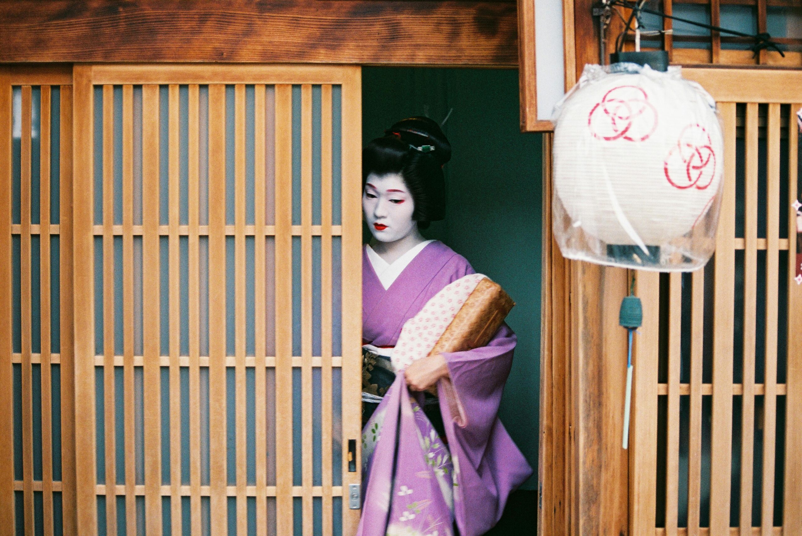 A Geisha dressed in a purple kimono steps out of a traditional Kyoto tea house, captured in a candid moment.