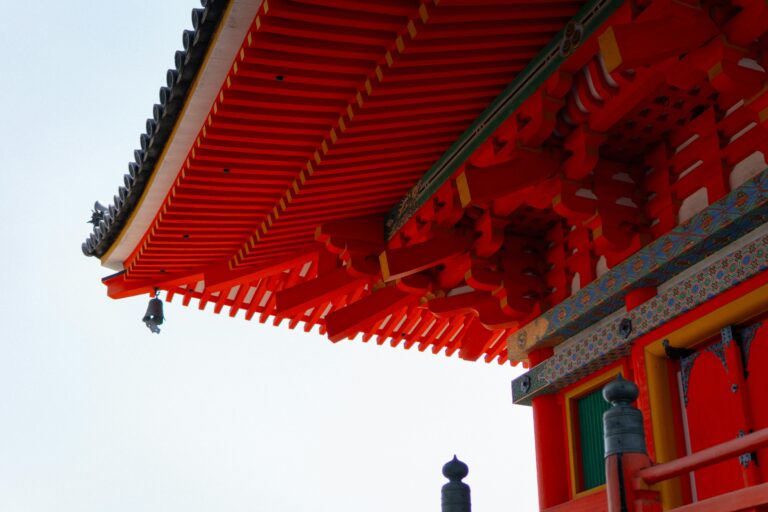 Close-up view of a vibrant red traditional Japanese temple roof with intricate wooden architectural design.