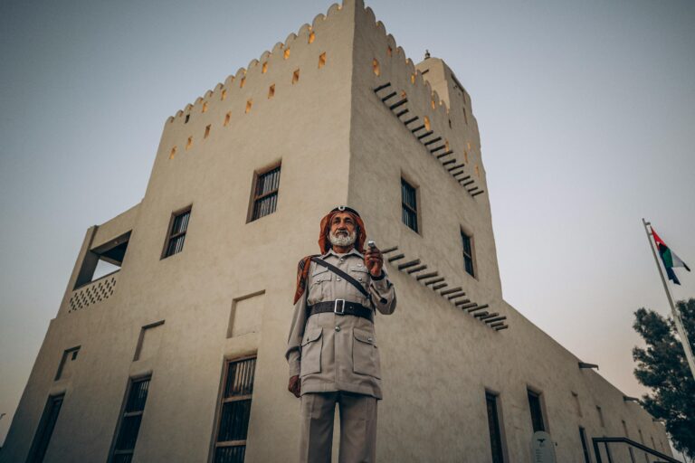 An Emirati guard in traditional attire stands before a historical building in Abu Dhabi.