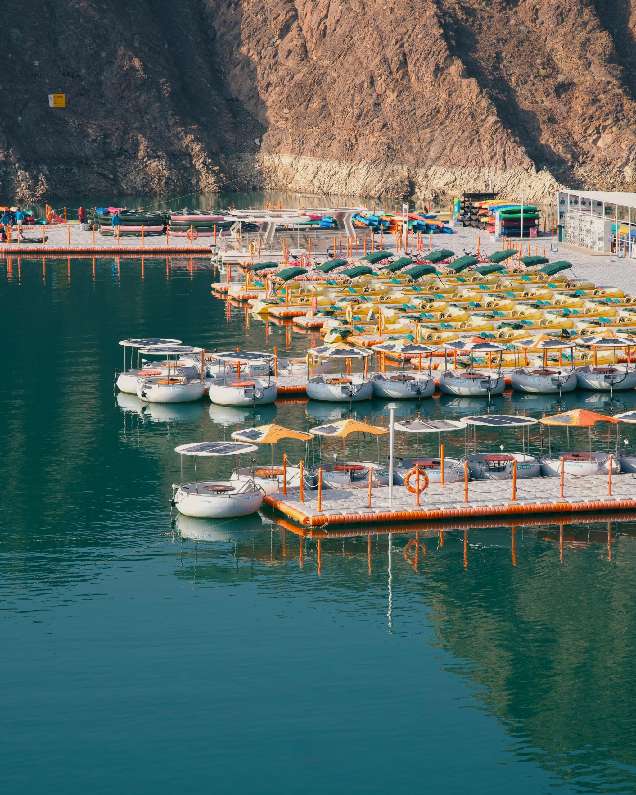 Colorful boats docked at Hatta Dam in Dubai, surrounded by rugged mountains and calm waters.