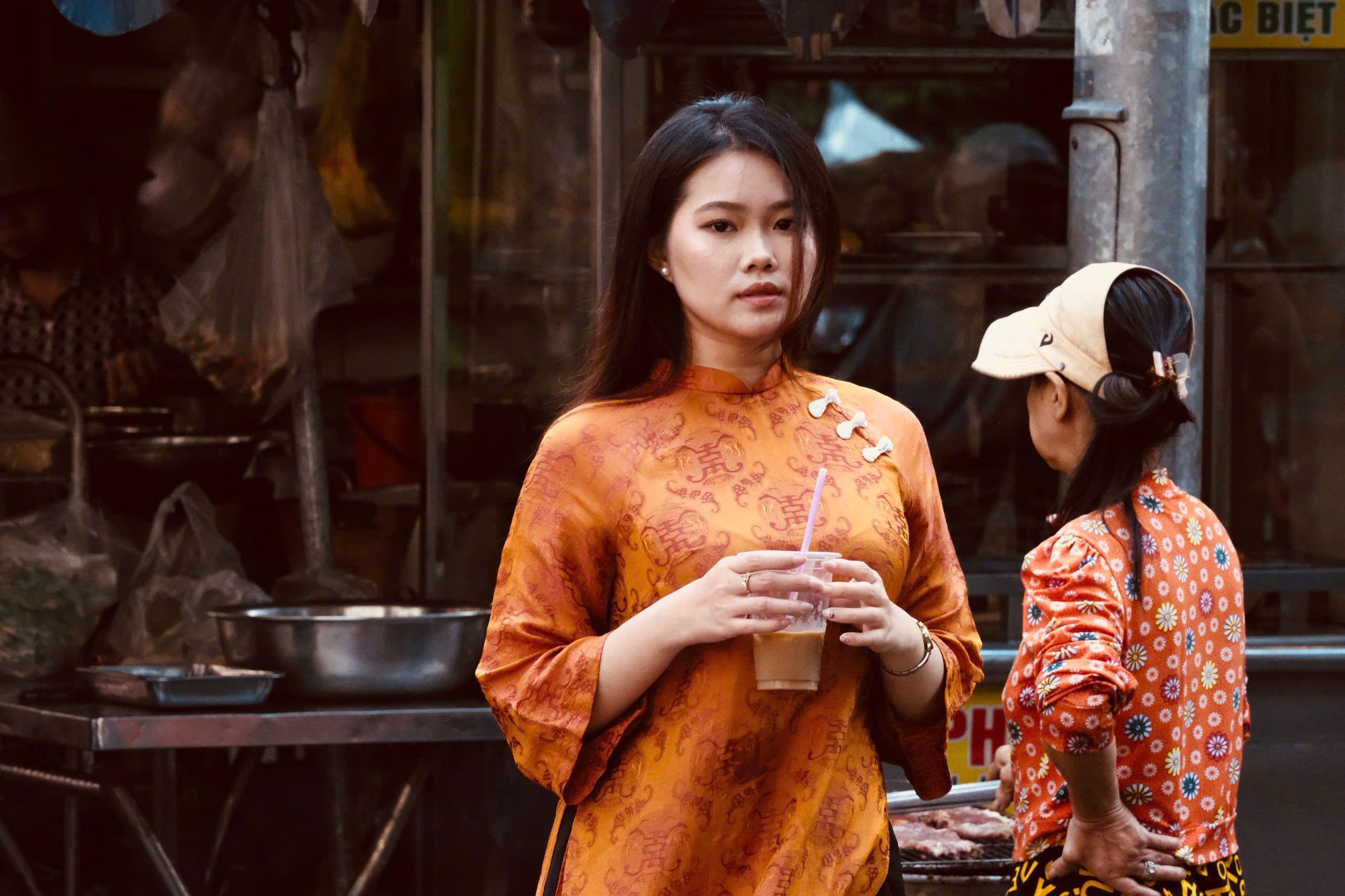 A young woman in an orange traditional dress holds a drink outdoors, adding cultural vibrancy.