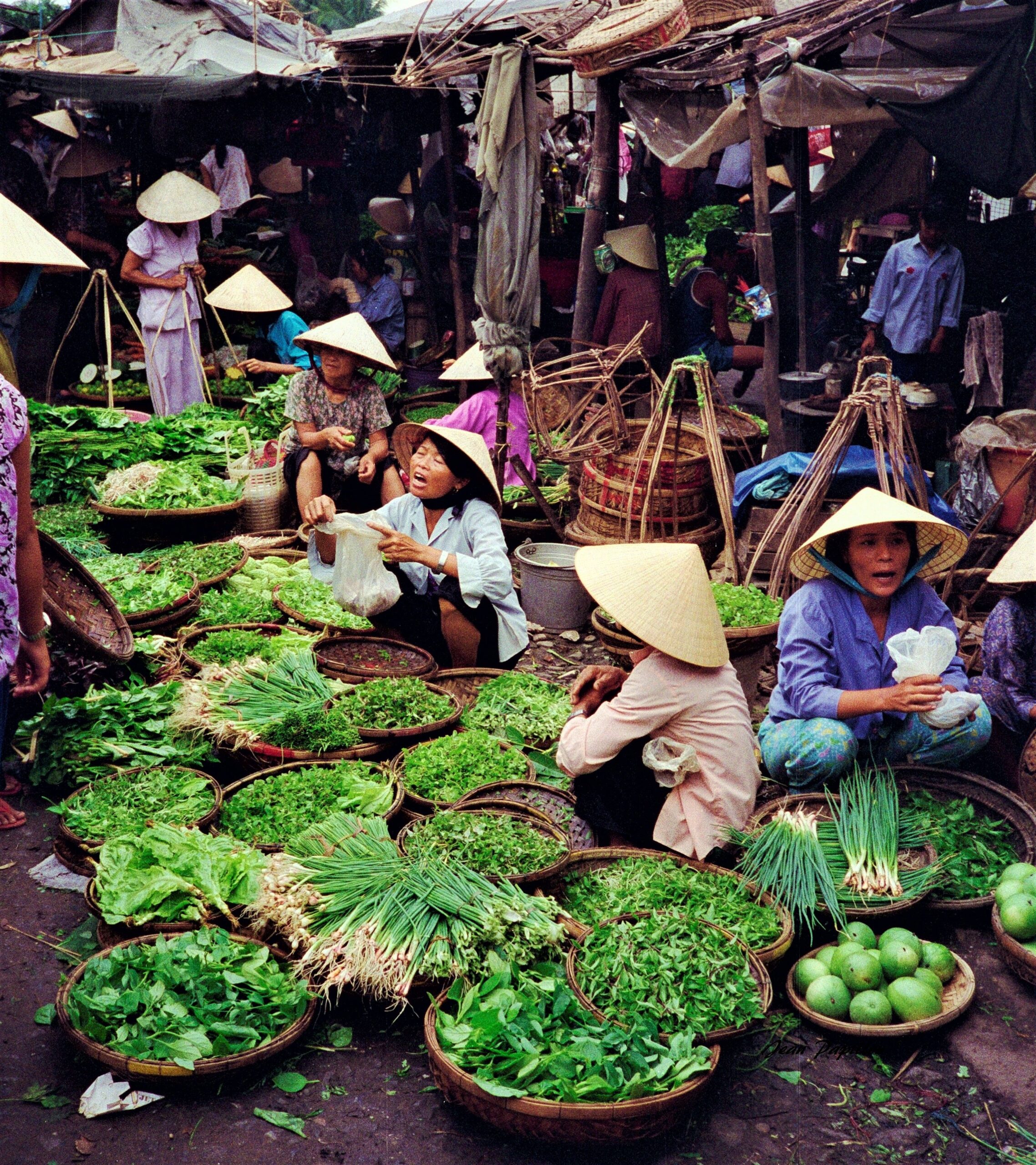 Vibrant street market in Hội An with vendors selling fresh vegetables wearing traditional hats.