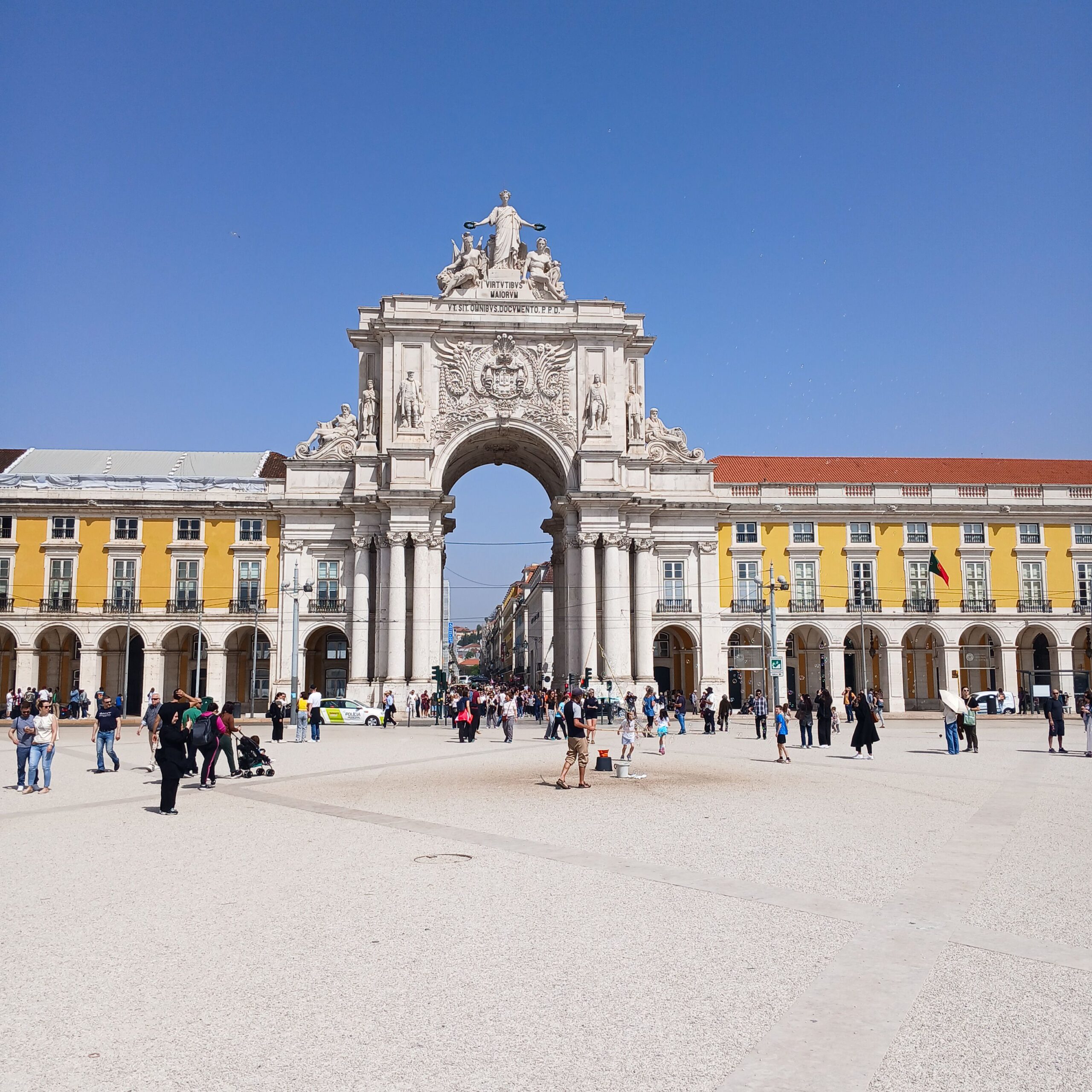 Crowd gathers at Rua Augusta Arch in sunny Lisbon, Portugal. Iconic architecture and vibrant city life.