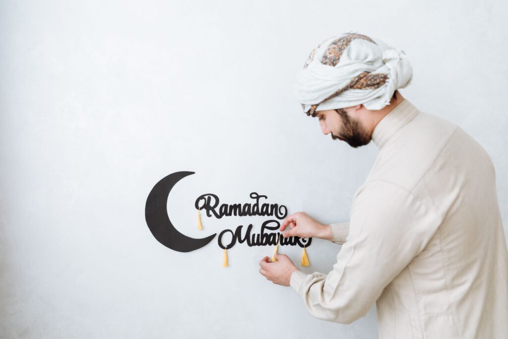 A man places a Ramadan Mubarak sign with decorative elements on a white wall.